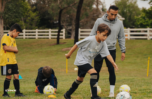 Coach francisco helping trilogy athlete Cole in his dribbling drill.